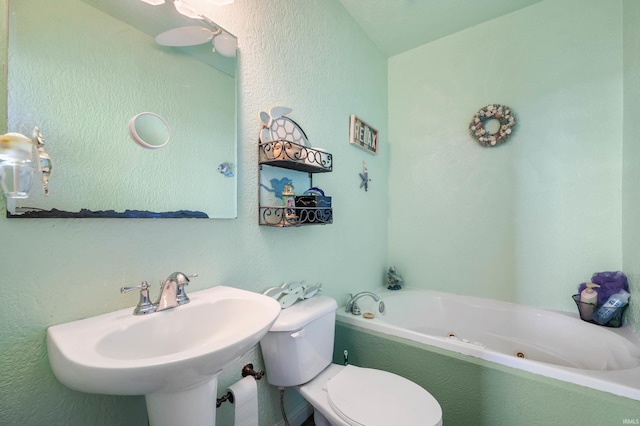 full bath featuring a jetted tub, toilet, a sink, and a textured wall