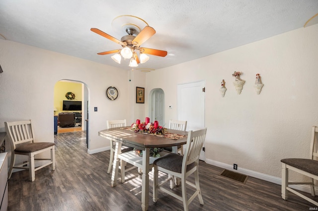 dining room featuring arched walkways, dark wood finished floors, ceiling fan, and baseboards