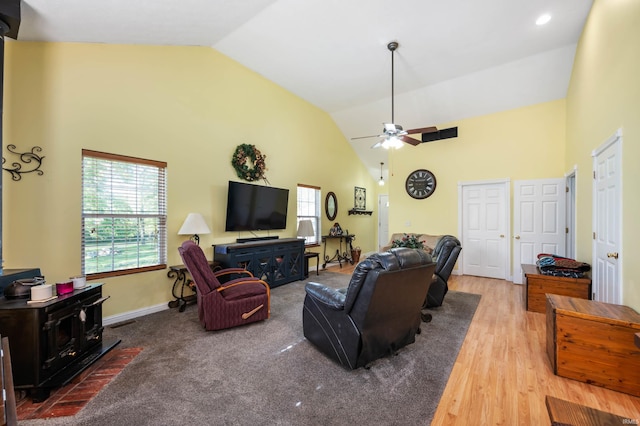 living area featuring a wood stove, high vaulted ceiling, a ceiling fan, wood finished floors, and baseboards