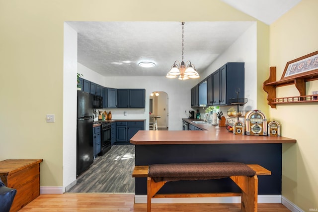 kitchen featuring arched walkways, black appliances, a peninsula, blue cabinets, and a sink