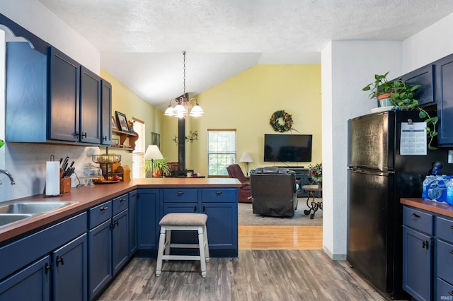 kitchen with freestanding refrigerator, a peninsula, a sink, dark wood-type flooring, and lofted ceiling