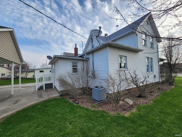 view of side of home featuring central AC unit, a yard, a chimney, and a patio