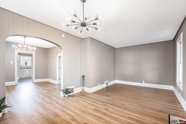 1614 Kendall St, South Bend, IN 46613 - spare room featuring a chandelier, arched walkways, light wood-type flooring, baseboards, and wood walls