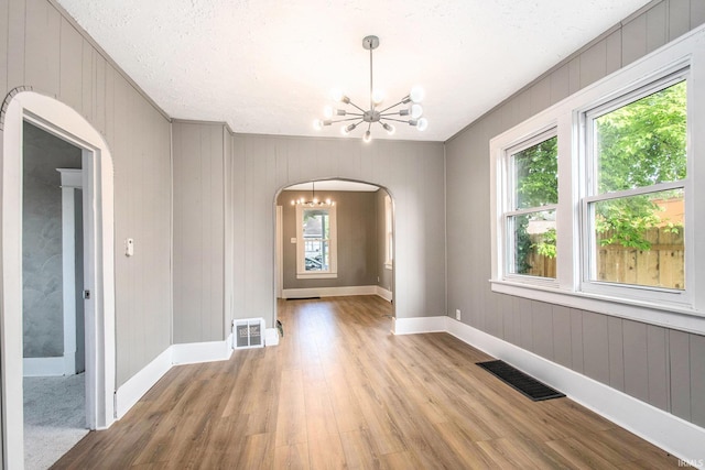 1614 Kendall St, South Bend, IN 46613 - spare room with arched walkways, a chandelier, light wood-style flooring, baseboards, and wooden walls