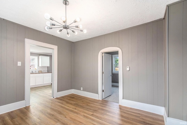 1614 Kendall St, South Bend, IN 46613 - empty room with arched walkways, a chandelier, light wood-style floors, baseboards, and wooden walls