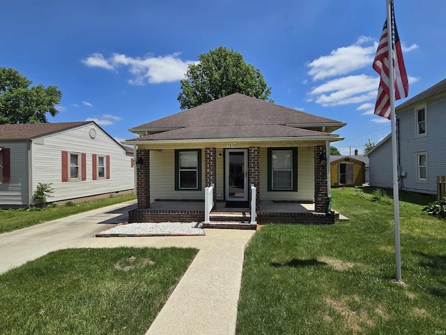 bungalow-style home featuring covered porch, a front yard, a shingled roof, and an outdoor structure