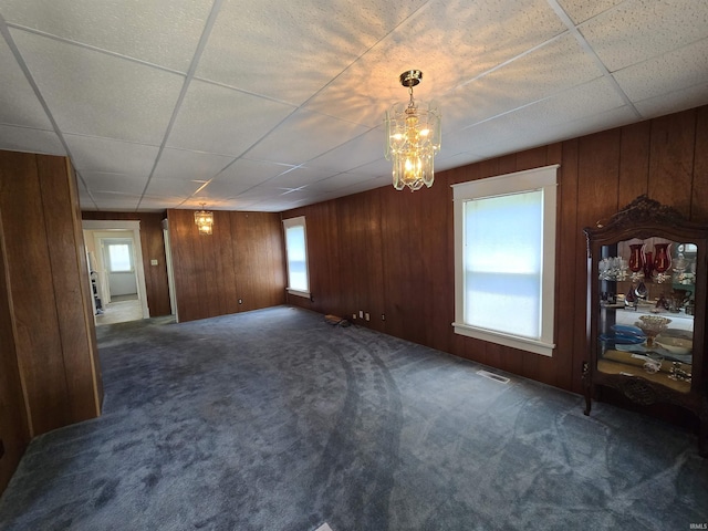 unfurnished living room with dark carpet, wood walls, and a paneled ceiling