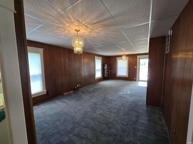 empty room with wooden walls, dark carpet, a chandelier, and a paneled ceiling