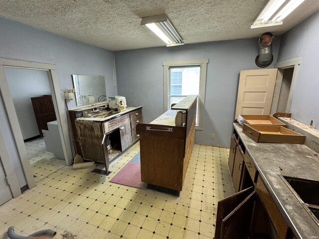 kitchen with light floors, a textured ceiling, dark brown cabinetry, and a sink