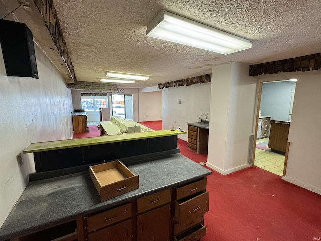 kitchen featuring a textured ceiling, dark colored carpet, dark countertops, baseboards, and dark brown cabinetry