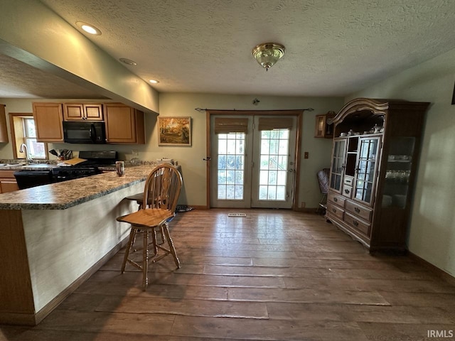 977 N Union Rd, Frankfort, IN 46041 - kitchen featuring black appliances, a textured ceiling, dark wood-style floors, a kitchen breakfast bar, and baseboards