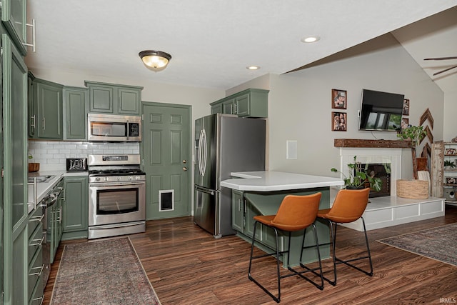 845 N Timberline Cir E, Warsaw, IN 46582 - kitchen with green cabinets, appliances with stainless steel finishes, a peninsula, dark wood finished floors, and a fireplace with raised hearth