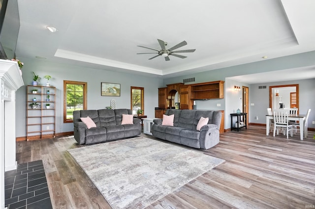 living area with a raised ceiling, ceiling fan, wood finished floors, and baseboards