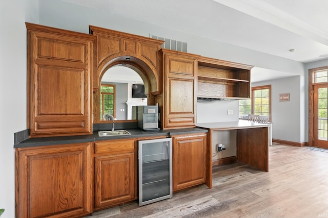 kitchen featuring beverage cooler, open shelves, light wood-style flooring, brown cabinets, and a sink