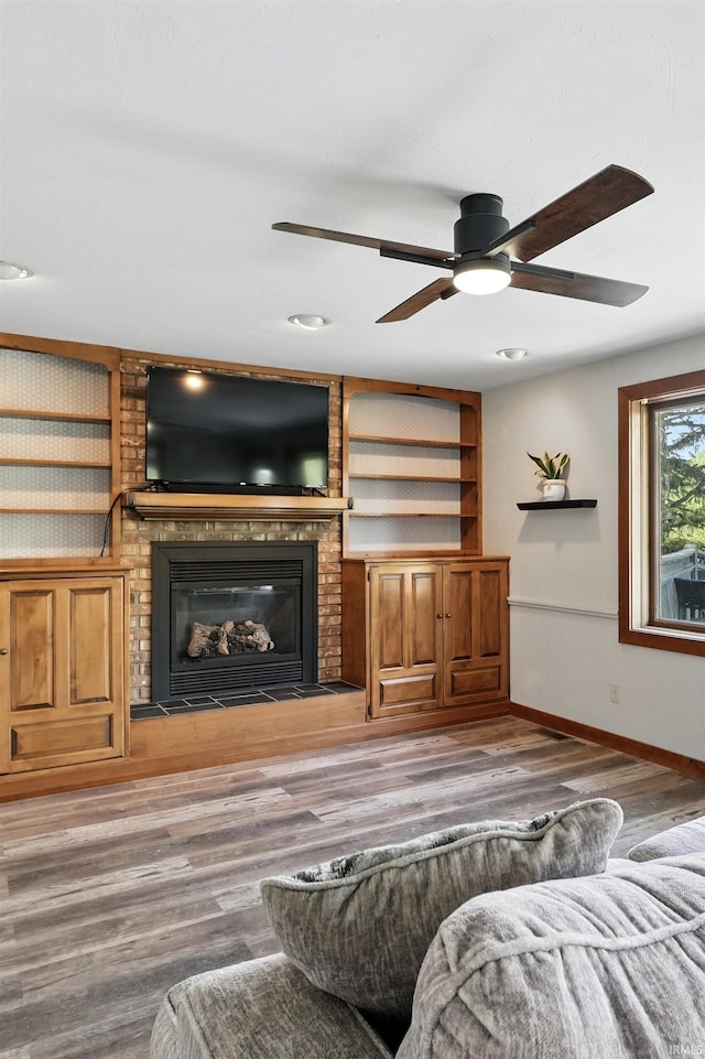 living room with baseboards, a fireplace, wood finished floors, ceiling fan, and built in shelves