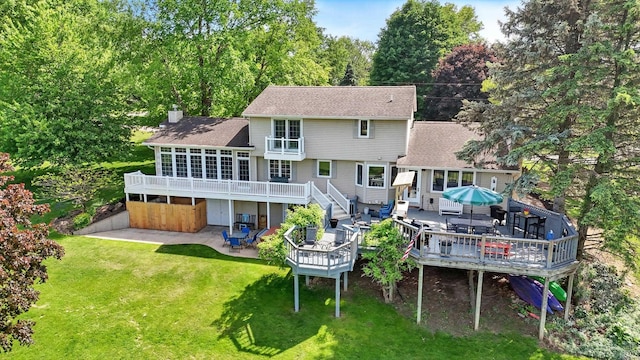 back of property featuring a deck, a patio, a chimney, and a lawn