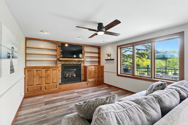 living area with baseboards, wood finished floors, ceiling fan, and a fireplace