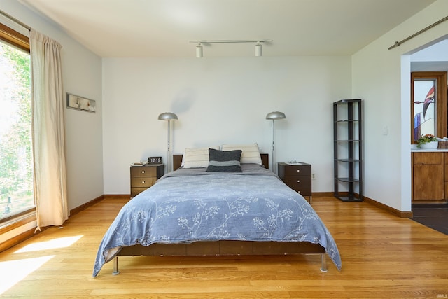 bedroom with light wood-type flooring, rail lighting, and baseboards