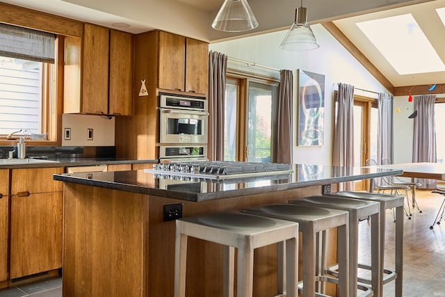 kitchen featuring a sink, stainless steel gas stovetop, dark countertops, brown cabinets, and a kitchen breakfast bar