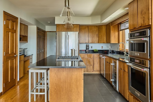 kitchen with a sink, stainless steel appliances, brown cabinets, dark countertops, and a kitchen island