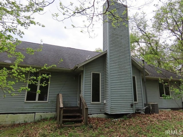 back of property featuring a chimney, central AC, and a shingled roof