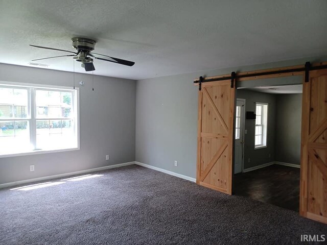 4020 N Fourth Ave, Evansville, IN 47711 - unfurnished room with a barn door, dark carpet, a ceiling fan, baseboards, and a textured ceiling
