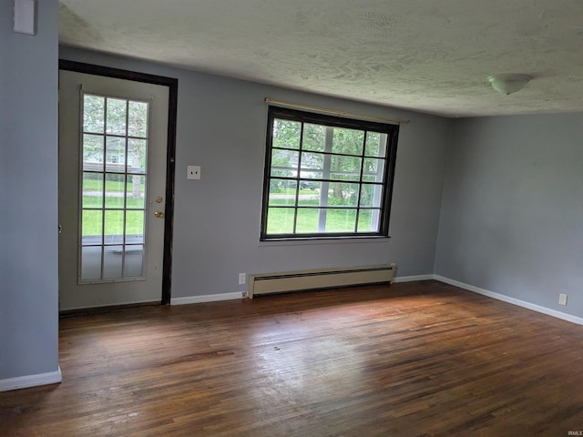 spare room featuring a baseboard heating unit, plenty of natural light, wood finished floors, baseboards, and a textured ceiling