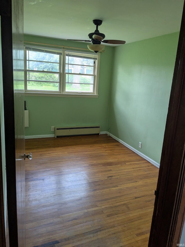 unfurnished room featuring a baseboard heating unit, ceiling fan, wood finished floors, and baseboards