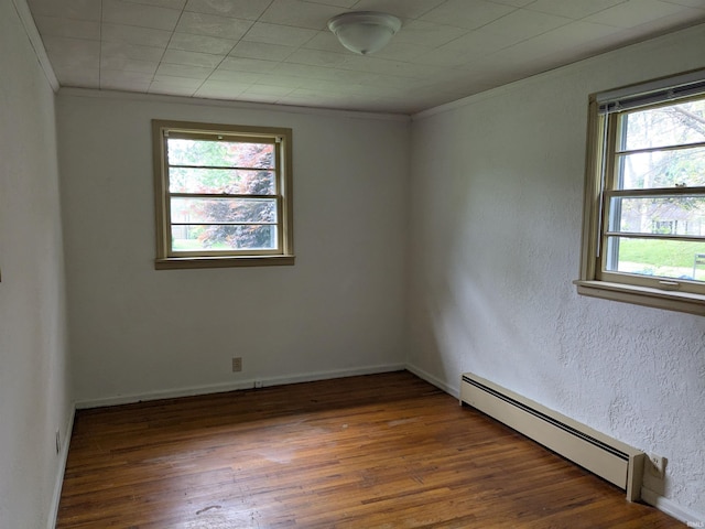 unfurnished room with a baseboard heating unit, wood finished floors, crown molding, and baseboards