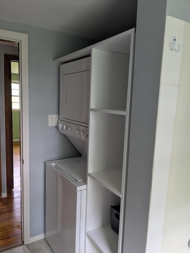 washroom featuring stacked washing machine and dryer, light wood finished floors, and baseboards