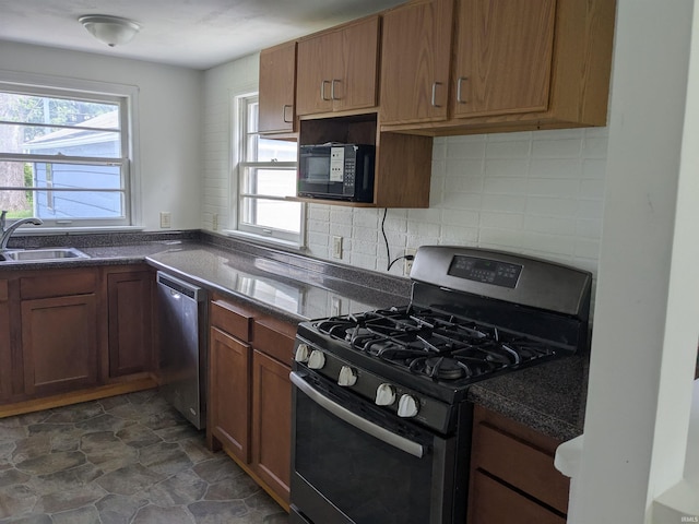 kitchen with stainless steel appliances, a sink, dark countertops, tasteful backsplash, and dark stone finish floors