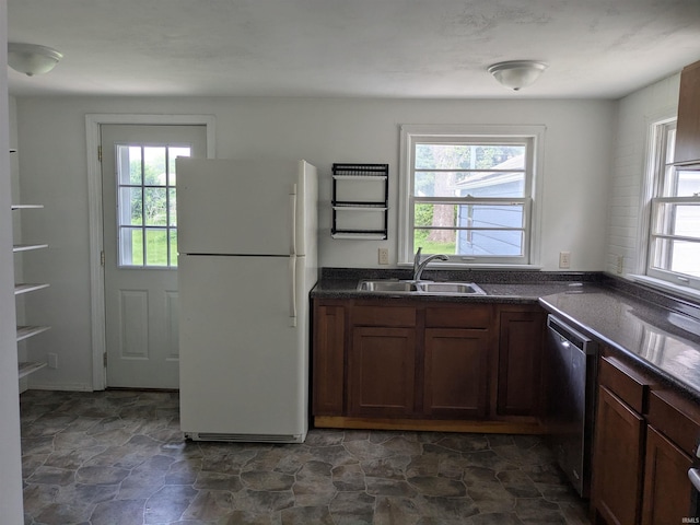 kitchen with freestanding refrigerator, a sink, dishwasher, and dark stone finish floors