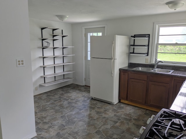 kitchen with freestanding refrigerator, a sink, dark stone finish flooring, and healthy amount of natural light