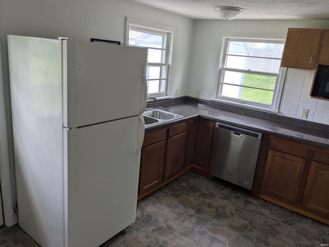 kitchen featuring freestanding refrigerator, dishwasher, dark countertops, a sink, and dark stone finish floors
