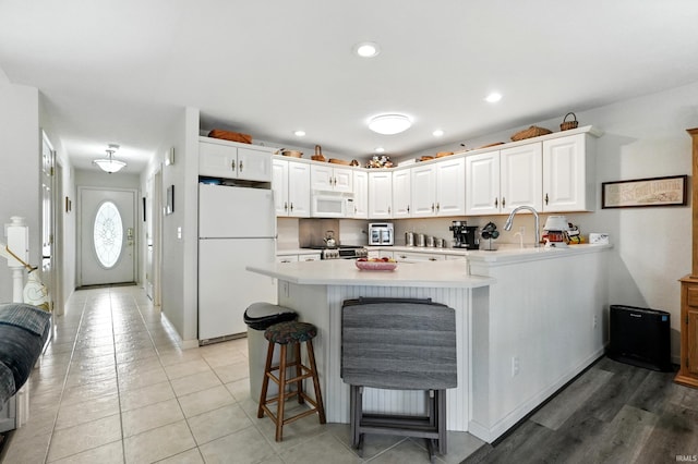kitchen featuring white appliances, a peninsula, light countertops, white cabinetry, and a kitchen breakfast bar