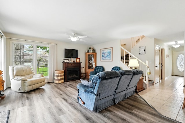 living room featuring stairway, ceiling fan, a fireplace, and light wood-style flooring
