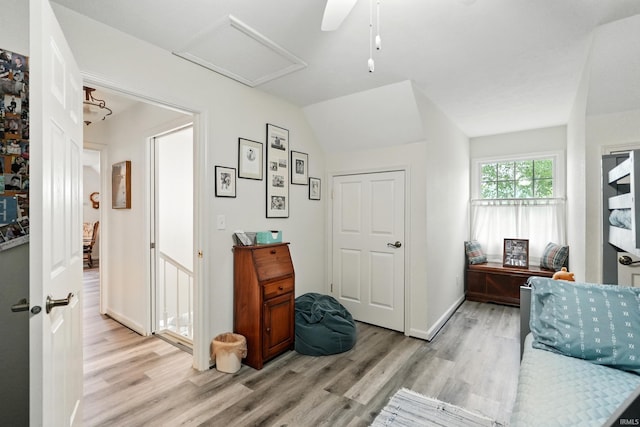 corridor with light wood-style flooring, attic access, baseboards, and vaulted ceiling