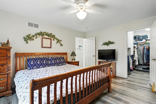 bedroom featuring light wood-style flooring, baseboards, a walk in closet, a closet, and ceiling fan