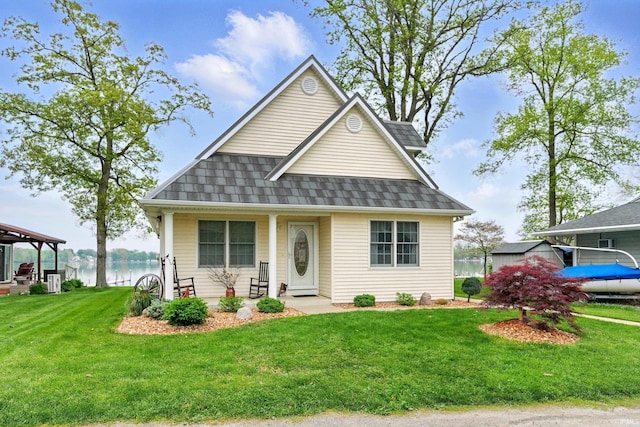 view of front facade featuring a front lawn, a porch, a water view, and a shingled roof