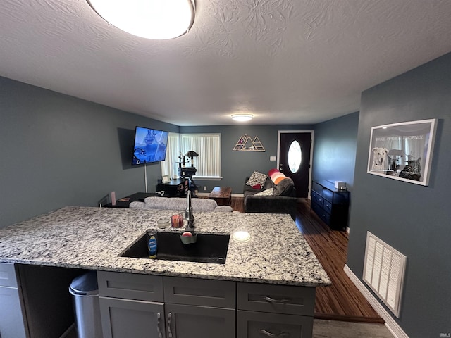 201 W Waid Ave, Muncie, IN 47303 - kitchen featuring open floor plan, dark wood-style flooring, light stone countertops, a center island with sink, and a textured ceiling