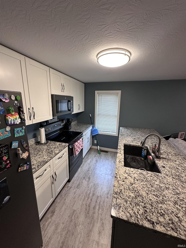 201 W Waid Ave, Muncie, IN 47303 - kitchen featuring black range with electric stovetop, freestanding refrigerator, a sink, white cabinetry, and a textured ceiling