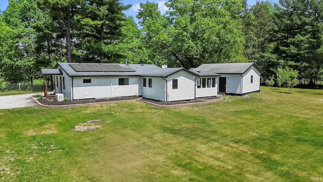rear view of property featuring solar panels, a lawn, and view of scattered trees