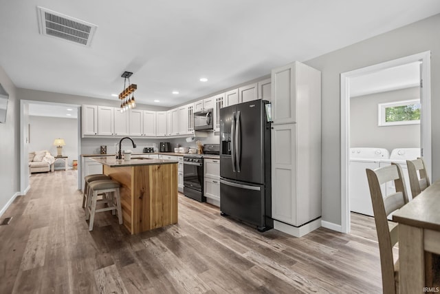 kitchen with black refrigerator with ice dispenser, range, stainless steel microwave, washer and clothes dryer, and a sink