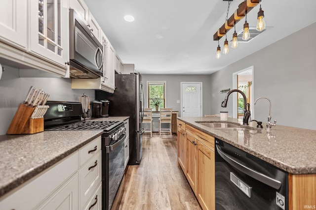 kitchen featuring dishwasher, gas stove, stainless steel microwave, light wood-type flooring, and a sink