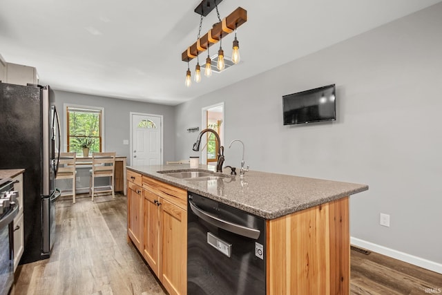 kitchen with stainless steel appliances, a sink, wood finished floors, a center island with sink, and light stone counters