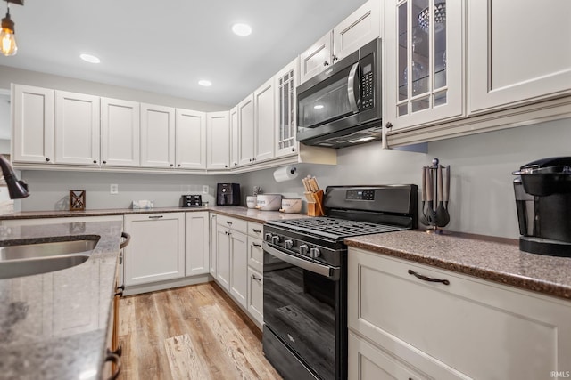 kitchen featuring black gas range oven, a sink, light wood-style floors, white cabinetry, and glass insert cabinets