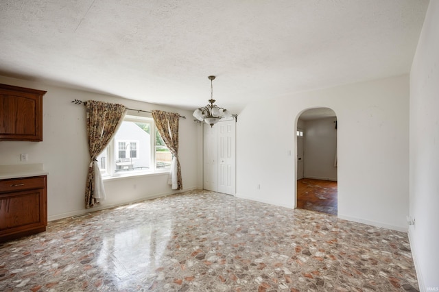 217 Vasbinder Dr, Anderson, IN 46017 - unfurnished dining area featuring arched walkways, a chandelier, a textured ceiling, stone finish floors, and baseboards