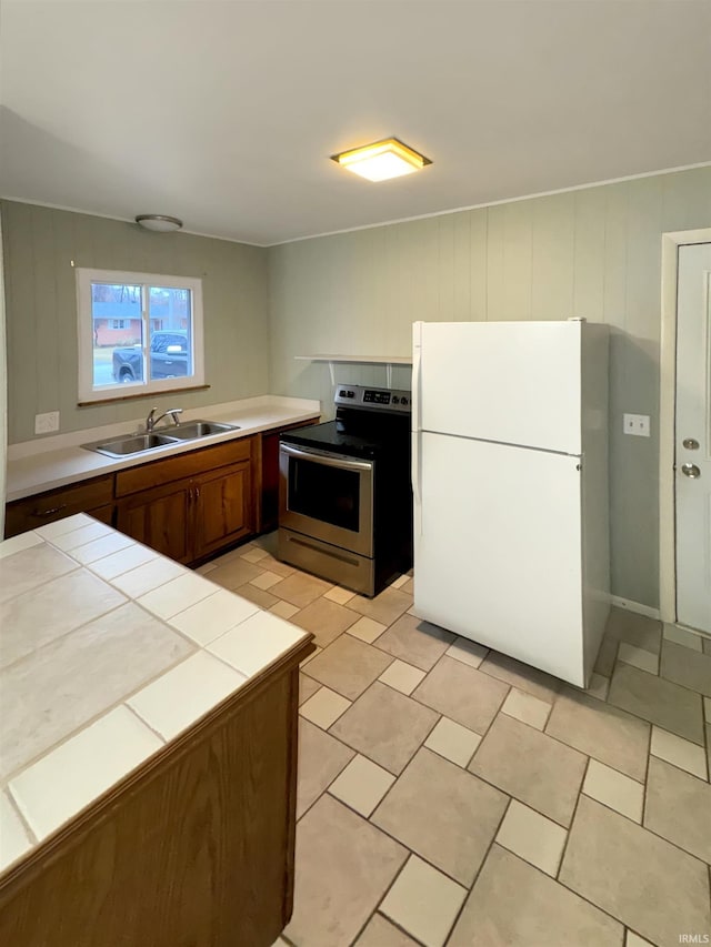 2301 E Delaware St, Evansville, IN 47711 - kitchen featuring stainless steel range with electric stovetop, a sink, freestanding refrigerator, tile countertops, and brown cabinets