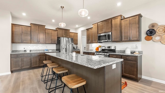 5263 Gadwall Pass, Fort Wayne, IN 46818 - kitchen with appliances with stainless steel finishes, a sink, light wood-style flooring, tasteful backsplash, and a kitchen breakfast bar