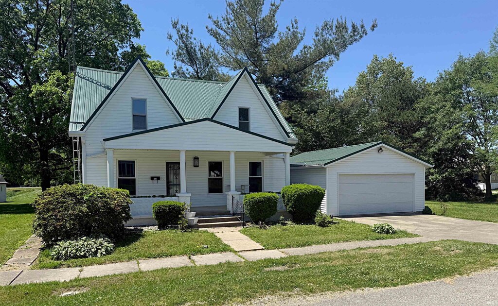 109 Mulberry St, Loogootee, IN 47553 - view of front facade with a garage, a front yard, covered porch, driveway, and metal roof